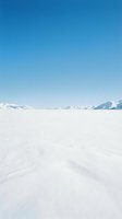 Vast snowy landscape with snow-covered mountains on horizon under clear blue sky. Minimalist winter scenery for travel, nature, and seasonal design projects.