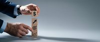 Businessman hands stacking wooden blocks with business icons including dollar sign, growth arrow and target symbols representing strategic planning and success.