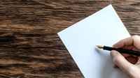 Hand holding fountain pen over blank white paper on rustic wooden table background, ready for writing letter, note or creative content.