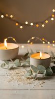 Cozy candles burning in ceramic holders with eucalyptus leaves and warm fairy lights creating peaceful spa atmosphere for relaxation and wellness.