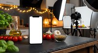 Food photography setup with smartphone mockup, professional lighting equipment and fresh ingredients on kitchen counter for content creation.
