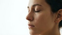 Young woman with closed eyes and tears streaming down face showing raw emotion and vulnerability in soft natural lighting for mental health concepts.