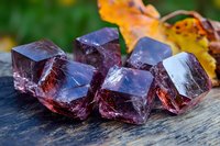 Raw purple fluorite crystal specimens on rustic wooden surface with autumn leaves in background, showcasing natural mineral formation and transparency.