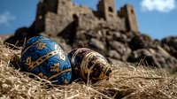 Decorated Easter eggs with intricate patterns lying on straw with ancient medieval castle ruins in soft focus background creating atmospheric holiday composition.