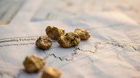 Gold nuggets scattered on financial newspaper with market charts showing commodity trading and precious metals investment analysis.