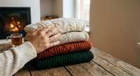 Cozy stack of warm knitted sweaters on wooden table by fireplace creating comfortable autumn winter home atmosphere for seasonal fashion storage.