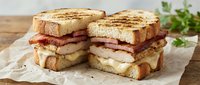 Grilled sandwich with bacon, cheese and turkey on toasted bread served on parchment paper. Perfect for cafe menus, food blogs and restaurant promotions.