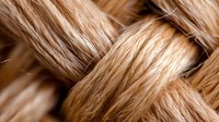 Macro shot of blonde braided hair strands intertwined in detailed pattern showing texture and natural highlights against soft brown background.