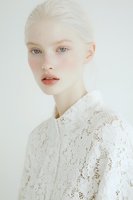 Young Caucasian woman with platinum blonde hair and freckles wearing white lace top against neutral background for fashion and beauty concepts.
