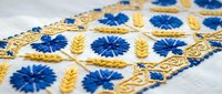 Traditional Ukrainian embroidery with blue cornflowers and golden wheat ears on white linen fabric showcasing folk art craftsmanship and cultural heritage.