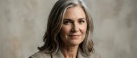 Mature woman with long gray hair and fair complexion smiling at camera against neutral background, suitable for healthcare, wellness, lifestyle and corporate business applications.