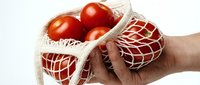 Hand holding a reusable cotton mesh bag filled with fresh red tomatoes, promoting eco-friendly grocery shopping and zero waste lifestyle.