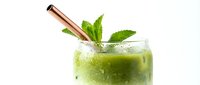 Fresh green smoothie in a frosty glass with a rose gold metal straw and mint leaves, isolated on white background.
