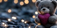 Gray teddy bear holding burgundy heart against blurred bokeh lights background, romantic mood setting for Valentine's day or love concepts.