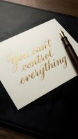Elegant gold calligraphy quote on white paper with fountain pen on dark leather surface for motivational and inspirational design projects.