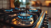 Close up view of blue gas stove flame burning on modern kitchen cooktop with dark metal surface, showing energy consumption and cooking preparation.