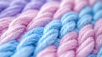Soft pastel colored yarn in diagonal rows featuring pink and blue tones with gentle twisted texture creates calming craft background pattern. Macro close up view.