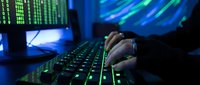 Hacker typing on illuminated keyboard in dark room with multiple monitors displaying code and data streams for cybersecurity concepts.