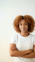 Confident young African American woman with curly hair crossed arms wearing white t-shirt smiling at camera against neutral background for lifestyle content.