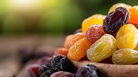 Colorful assortment of dried fruits including dates, apricots, raisins and figs in rustic wooden bowl on natural background for healthy snacking and cooking.