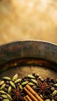 Wooden bowl filled with cardamom pods, star anise, cinnamon sticks, and allspice berries on warm blurred background. Culinary and spice photography.