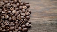 Fresh roasted coffee beans scattered on rustic wooden table with copy space, macro shot showing rich texture and natural brown tones. Perfect for cafe marketing.