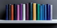 Colorful hardcover books arranged in row on white shelf against dark background, creating minimalist composition with vibrant spines in various hues.