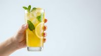 Refreshing lemonade with mint and lemon slices in tall glass held by hand against white background. Summer drink for healthy lifestyle and hydration.