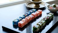 Colorful sushi rolls arranged in neat rows on dark slate plate with traditional Japanese serving dishes and tea set in elegant restaurant setting.