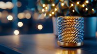 Glowing candle holder with textured metallic surface creates cozy atmosphere against blurred Christmas lights background, perfect for holiday decor and ambiance.