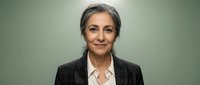 Professional mature Hispanic businesswoman with gray hair in dark suit smiling confidently against green background for corporate headshot and leadership content.