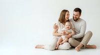 Happy young family with baby sitting together on floor wearing neutral clothing against white background for lifestyle photography.
