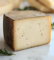 Aged cheese wedge with dark rind and creamy interior on marble surface, garnished with fresh rosemary sprig, macro food photography for culinary use.