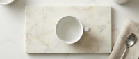 Empty white ceramic cup on marble cutting board with spoon, overhead flat lay composition for kitchen, dining, and tableware design projects.