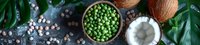 Fresh green peas in wooden bowl with chickpeas, coconut halves and tropical leaves on dark background. Healthy vegan protein sources.