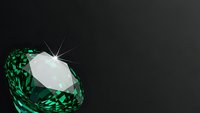 Emerald green gemstone with brilliant cut facets reflecting light on dark background for luxury jewelry and precious stone designs.