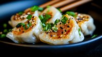 Asian dumplings garnished with sesame seeds, green onions and sauce on black plate, close up view showing texture and filling for food service.