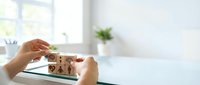 Woman hands arranging wooden blocks with family icons on white desk in bright modern office interior for family planning and life insurance concepts.