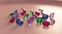 Collection of colorful precious gemstones including emeralds, sapphires, rubies and amethysts scattered on reflective surface for jewelry design.