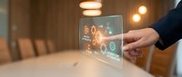 Businessman hand holding transparent digital tablet displaying glowing orange network icons and gears, representing technology, connectivity, and business solutions in modern office environment.