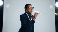 Professional African American businesswoman in glasses launching paper airplane in modern office with bokeh lights background for corporate success concepts.