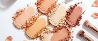 Assorted powder swatches in warm nude and bronze tones with makeup brushes on white background for cosmetics and beauty product marketing.