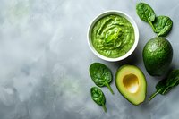 Fresh avocado dip with spinach leaves and ripe avocado half on gray concrete background. Healthy green sauce for Mexican cuisine and snacks.