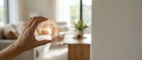 Close-up of hand holding glowing light bulb against blurred interior background, symbolizing innovation, ideas, energy efficiency and sustainable solutions for home and business.