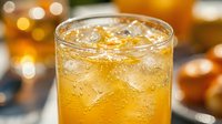 Refreshing iced orange drink in a glass with ice cubes and bubbles, golden bokeh background, summer beverage concept.