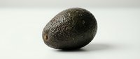 Whole dark green avocado with textured skin isolated on white background, ready for food and culinary design projects.