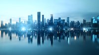 Modern cityscape with illuminated skyscrapers reflecting in calm water at dusk, creating mirror effect in blue tones. Urban waterfront panorama shows metropolitan skyline.