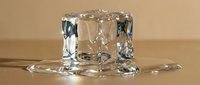Melting ice cube on a reflective surface with water puddle, showcasing transparency and light refraction on a warm beige background.