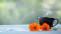 Steaming black coffee cup with bright orange poppies on lace doily against soft bokeh background, creating serene morning atmosphere.