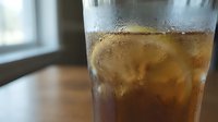 Chilled iced tea with lemon slices in a condensation-covered glass on a wooden table near a bright window.